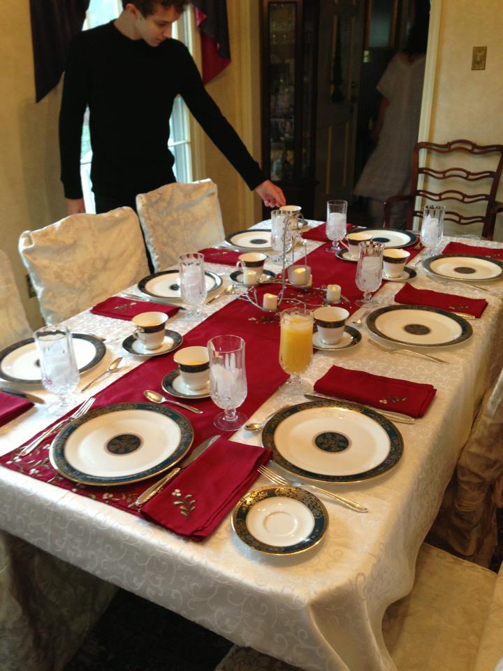 Table set for Christmas dinner with china and a red table runner.