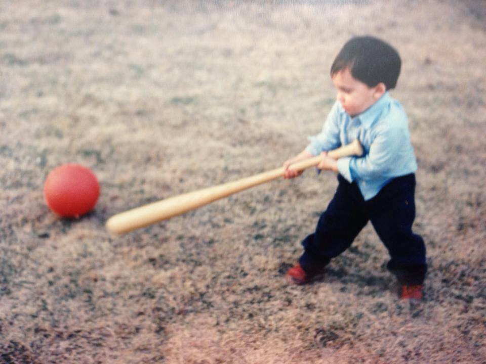 A confused three year old attempting to golf with a baseball bat using a basketball.
