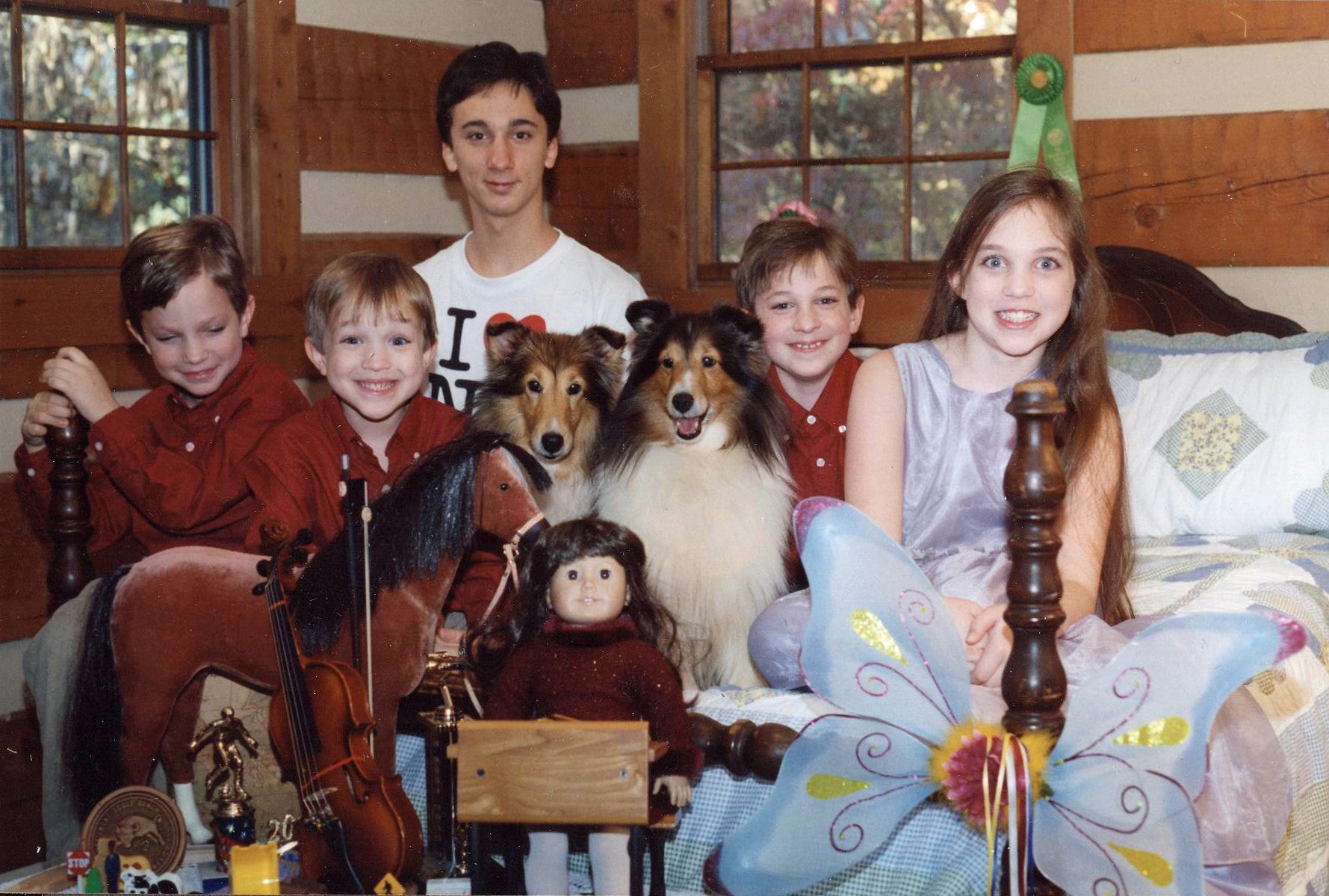 Children dressed for Christmas with their dogs and toys on a bed in a room in a log cabin.