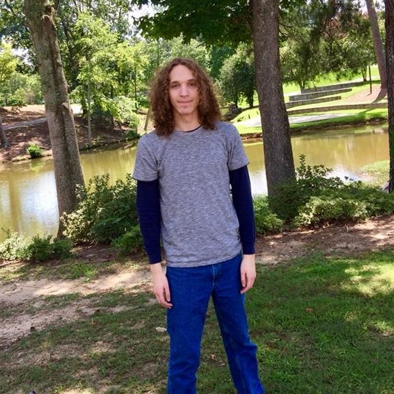Teenager at his first day of college. Long hair standing by a lake.