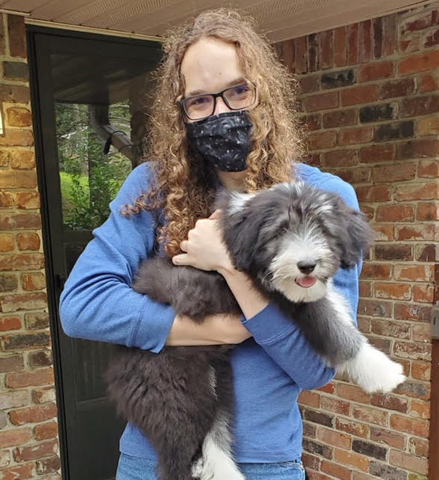 A young man in his early twenties holding a bearded collie puppy