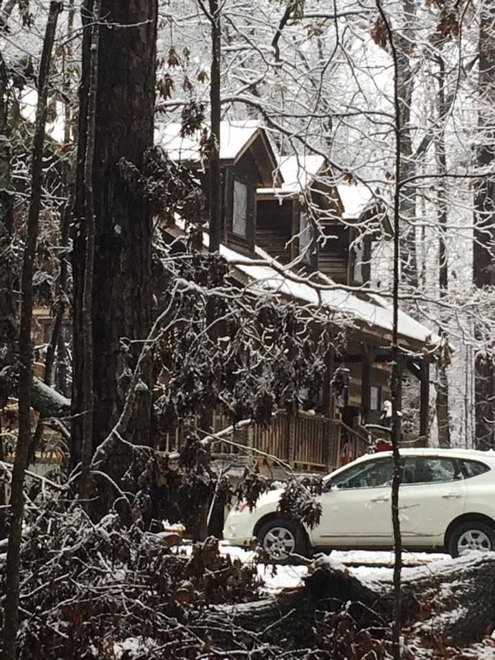 Log cabin in the snow with cars parked out front.