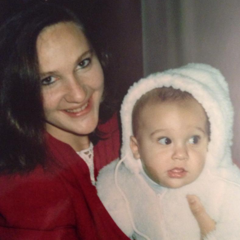 A young mother dressed in a red wool suit holding a baby in a white snow suit